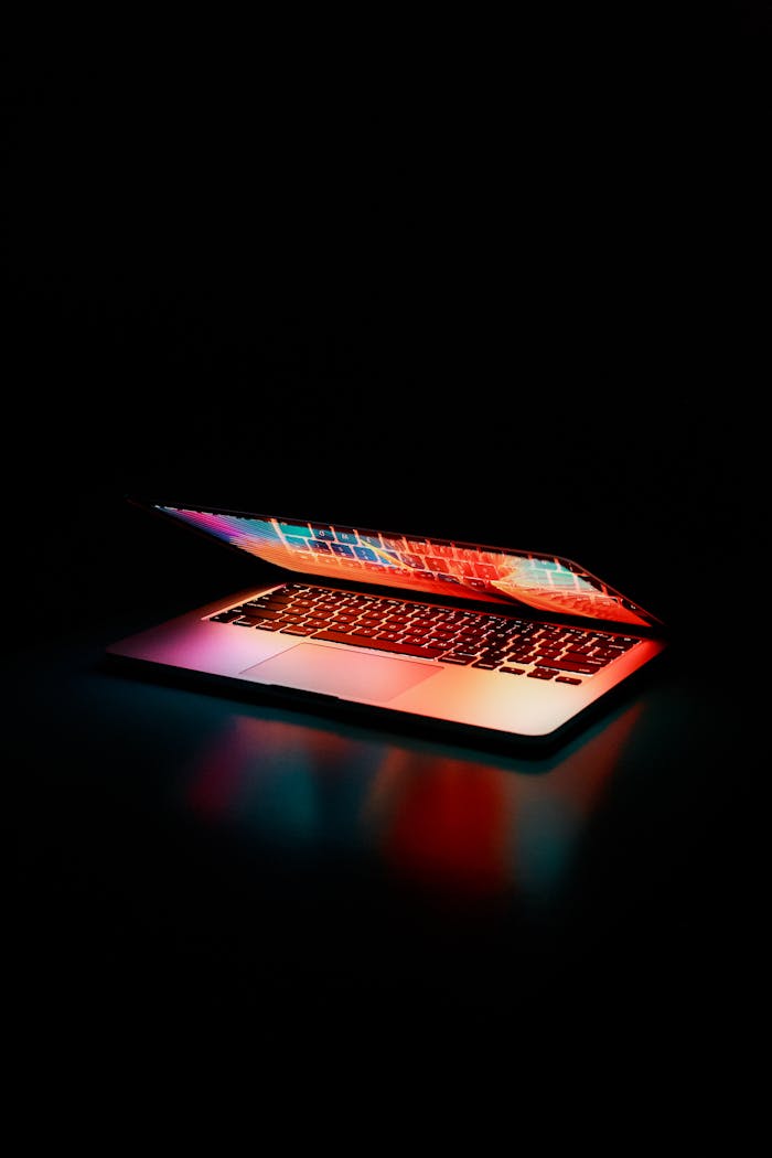 creative Laptop partially opened, emitting vibrant multicolored lights in dark setting.