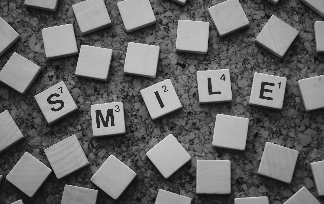 Monochrome image of Scrabble tiles forming the word 'Smile' on a textured surface.